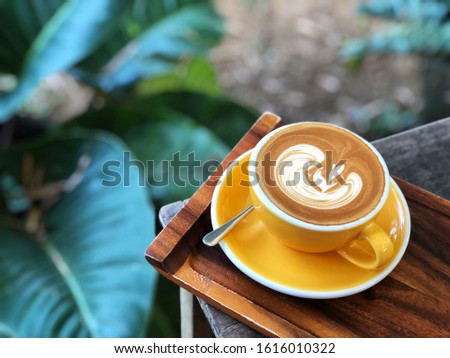 Cup of love , heart shape latte art coffee in yellow and white cup on the vintage wooden table with  green garden background . Love coffee love in your cup. 