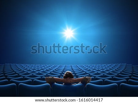 Empty blue cinema with VIP sitting in center and looking on bright screen. Mixed media. Royalty-Free Stock Photo #1616014417