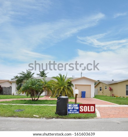 Sold Real Estate Sign On Front Yard Lawn Suburban Ranch Style Home in Residential Neighborhood Blue Sky Clouds USA