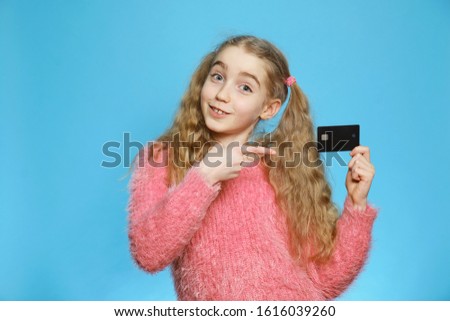 Little girl with a bank card. Joyful girl isolated on a blue background.  Isolated half-length portrait. The concept of savings, deposit.