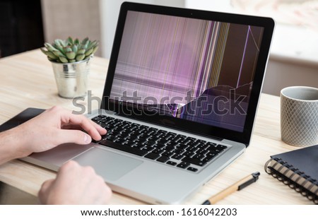 Broken laptop repair, insurance concept. Man working with a computer with damaged screen, office business background.