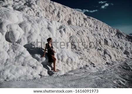 Surrealistic photo of a young beautiful girl in a black dress standing by the Pamukkale natural pool with space in the background
