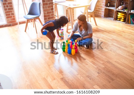 Beautiful teacher and toddler girl playing bowling at kindergarten