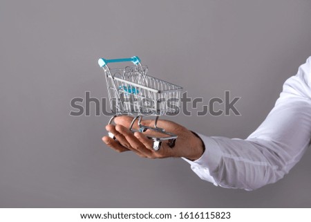 Closeup photo of a mini shopping cart while a man holding it in a white shirt in front of a grey background in the studio.
