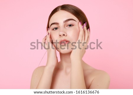 Beautiful young girl touching her perfect skin on pink background. Skin care concept. Beauty Woman Portrait with clean skin. Beauty cute fashion model with natural make up on pink background