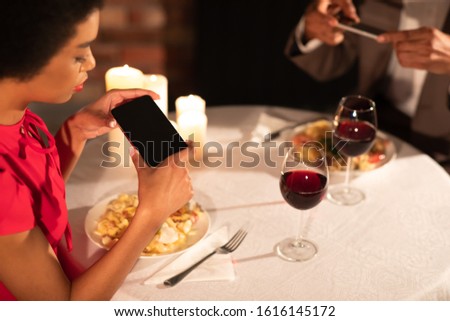 Modern Relationship. Millennial Afro Couple Taking Photo Of Food On Phones During Romantic Dinner In Fancy Restaurant. Cropped, Selective Focus