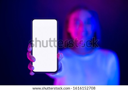 Cool app. Girl showing phone with blank screen in neon lights, free space