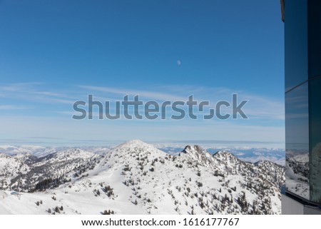 The moon and mountains viewed from top of Hidden Peak in winter at Snowbird Ski Resort in Little Cottonwood Canyon in the Wasatch Range near Salt Lake City, Utah, USA.