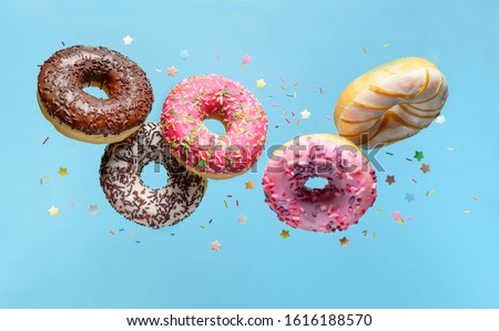Flying donuts. Mix of multicolored doughnuts with sprinkles on blue background. Royalty-Free Stock Photo #1616188570