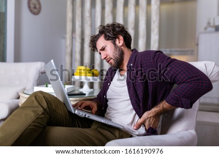 Tired man freelance worker stretch in sofa suffer from sitting long in incorrect posture, male employee have back pain or spinal spasm working in uncomfortable position. Sedentary life concept