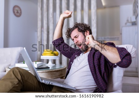 Tired man yawning after long working day . Early morning working. Sleepy tired freelancer is yawning at his home in front of the laptop`s screen on desk top