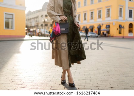 Trendy spring look. Fashion details. Woman Wearing beige coat and heels. Street on background. 