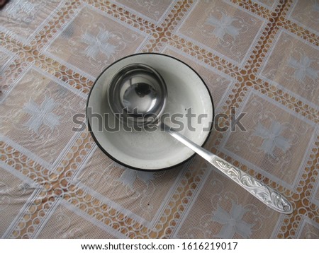 A round enamel soup Cup with a stainless steel ladle sits on the tablecloth of the dining table.