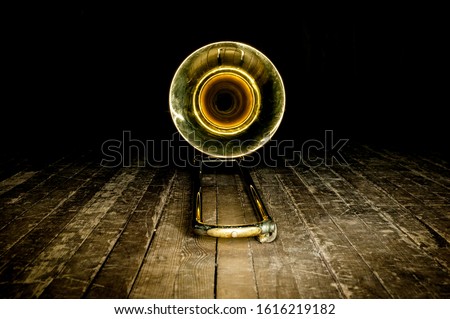 yellow brass instrument trombone lies on the wooden floor of the stage. front view on the bell Royalty-Free Stock Photo #1616219182