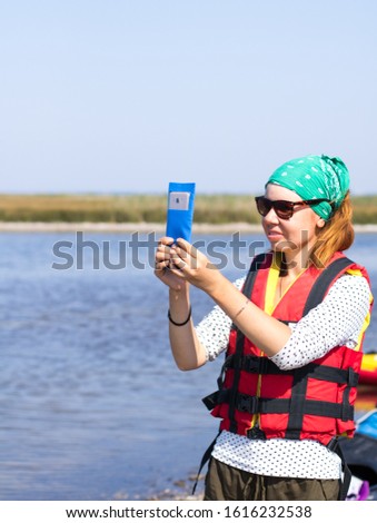 red-haired girl in red life vest taking photos on smartphone
