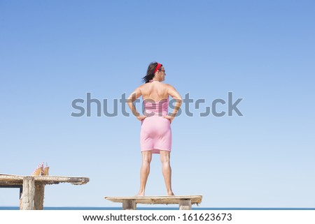 Portrait attractive mature woman standing confident and happy on table at tropical beach holiday, overlooking ocean, with horizon and blue sky as background and copy space.