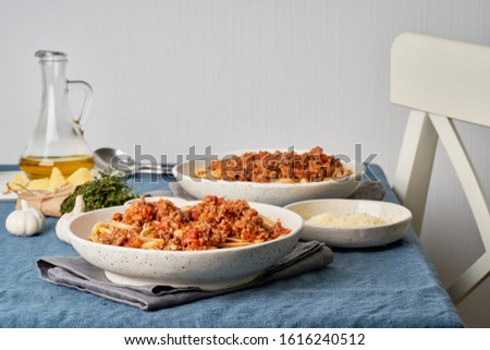 Pasta Bolognese Linguine with mincemeat and tomatoes. Italian dinner for two at the table, dark blue tablecloth, chair, homeliness. Side view Royalty-Free Stock Photo #1616240512