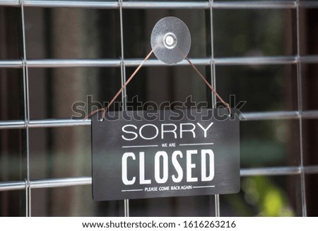 sorry we are close sign hanging on glass door of shop or restaurant with black steel shutter door. black wooden sign show text inform that shop is close, please come back again.