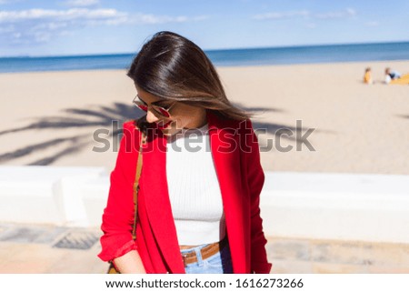 Young beautiful woman walking down the promenade by the beach, smiling and enjoying a sunny day