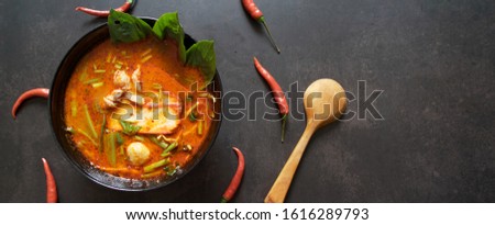 Panoramic banner for web, Thai food background concept. Dish of Thailand cuisine. Tom yum pork soup in black dish, rice in wooden plate on table dark background, space for text at right