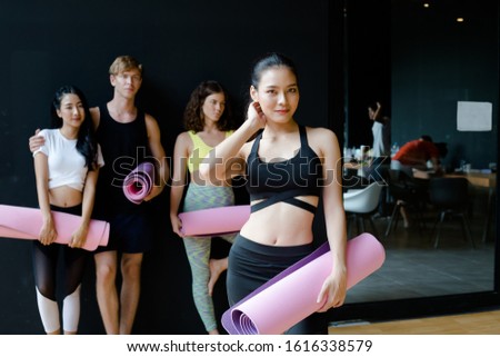 Portrait of Asian beautiful girl with black sportswear holding Yoga mat  after training yoga workout in studio room at gym fitness club.Have a good body shape and fit due to exercise and training yoga