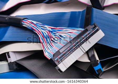 Colored multi wire parallel connector detail on ribbon cables pile. Flat insulated conductors for attachment of digital data storage device. White, blue or black textured strips. Computer spare parts. Royalty-Free Stock Photo #1616340364