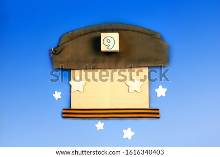 May 9. VICTORY DAY. St. George's ribbon, notebook, wooden stars, military cap. Color of the Year 2020. Blue background / Copy space for text. Defocused. Victory, memory, the concept of veterans.