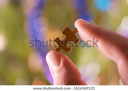 The fingers of a man hold a puzzle on a colorful background.