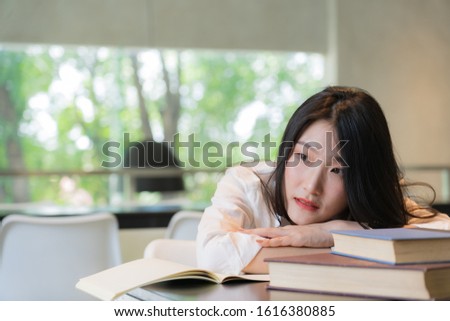 Beautiful student wearing white shirt resting while reading books on the table in library