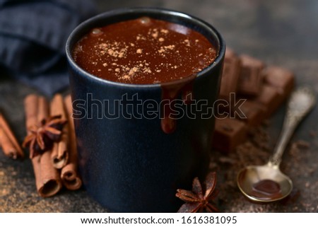 Delicious winter drink spicy hot chocolate with cinnamon and anise in a black cup on a dark slate, stone or concrete background.