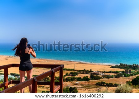 Young beautiful woman doing a picture with mobile phone. A woman is standing against a background of sea and mountains, she is a tourist