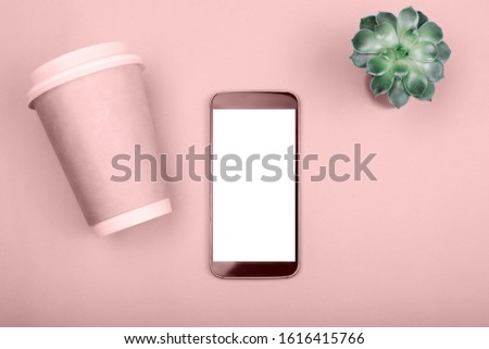 Smartphone white screen on pink table with disposable coffee cups and green flower