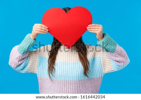 Be my valentine. Cute romantic shy girl in sweater hiding head behind red big heart sign, express love, confessing to friend, want start relationship showing sympathy and affection, blue background