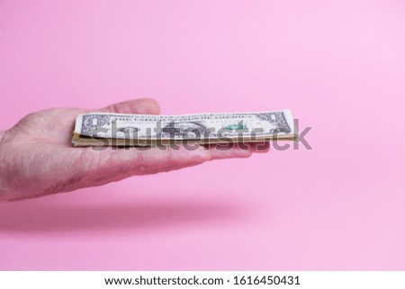 A bundle of dollar bills in a male hand on a pink background.