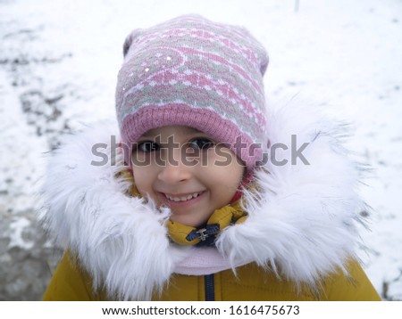 A girl in a winter jacket with white fluffy fur and a warm knitted hat on a background of snow.