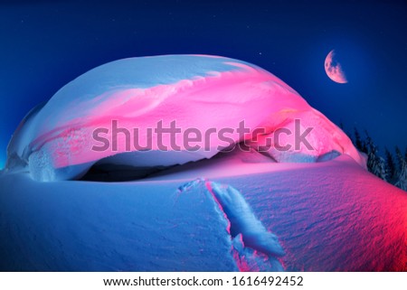 snow cornice at the top is a snow formation formed in the mountains under the influence of wind. Artistic illumination has created a fabulous fiction picture