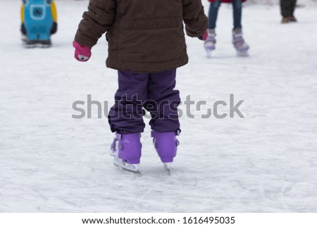 Back view of skates on child legs on rink in wintertime
