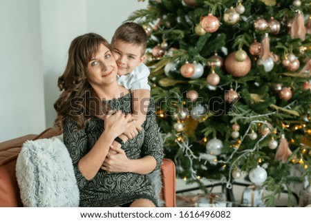 beautiful woman, mom with son, boy hugs mom, smiling and laughing, portraits on the background of a Christmas tree