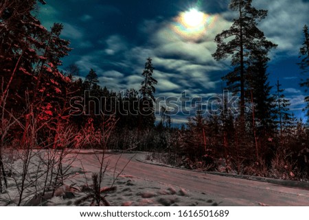 The moon shines on a road running along a winter forest. in the sky clouds and the remnants of the northern lights. red light from a leaving car