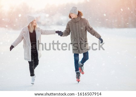 Loving couple in winter with skates on rink on sunset background, guy and girl dressed in warm hat.