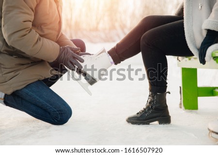 Man helps to put on white figure skates for rink to beautiful young girl on background of snow in winter, concept is care love, relationship between people.