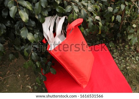 Blank 2020 Trends Lush Lava Color Shopping Bag Isolate on Hot Red Color Table against fresh natural green plant. Fabric Non Woven Bag. Recyclable ECO Friendly Bag. Lush Lava Color Code #FF4500