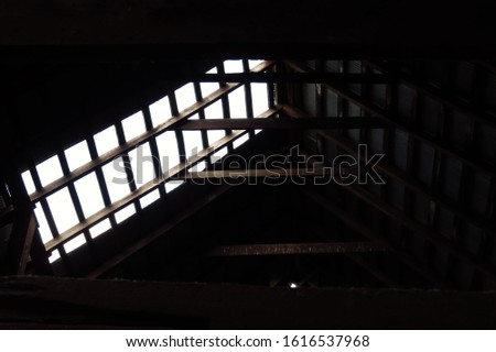 An open patch in the roof of an old barn with the bare wooden slats and beams showing. 