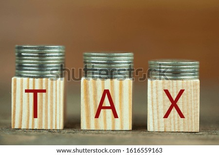 cubes with the word tax and coins are placed on a wooden surface