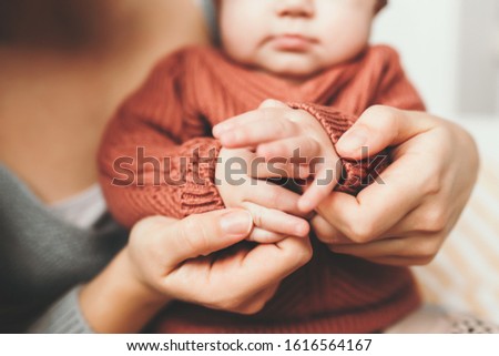 Young mother holding the handles of her little daughter, close-up, little fingers, concept of motherhood, cozy sweater. Mother with her newborn baby care hands
