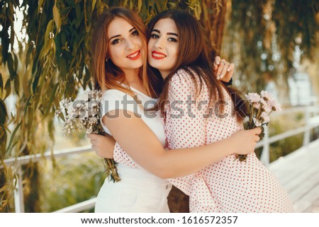 Beautiful girls with bouquet of flowers. Friends have fun in a summer park