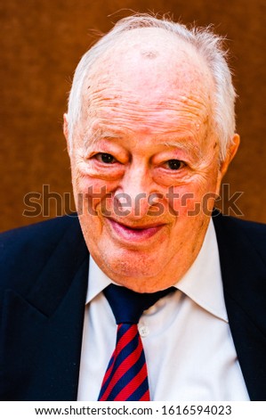 Portrait of happy white elderly man with dark suit, white shirt and striped blue red tie smiling on bright brown background Royalty-Free Stock Photo #1616594023