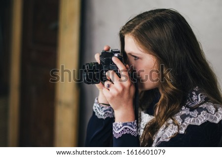 Young girl with a vintage camera takes photo. She adjusts the camera. Woman sets old camera for work. Girl in school uniform looks through viewfinder. Beautiful photographer poses with a camera