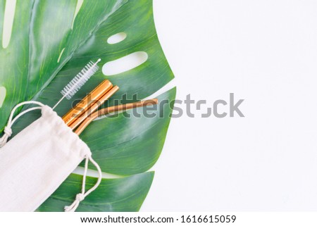 metal cocktail straws, a tube cleaning brush and an eco-friendly bag on a monstera leaf, the concept of zero waste and an eco-friendly lifestyle