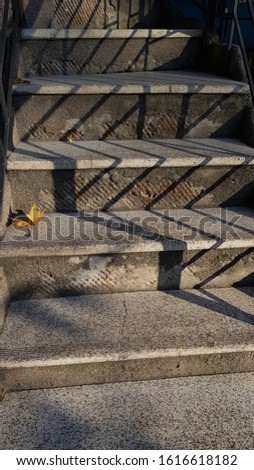 Old weathered stone staircase and striped shadows on dusty step surface. Dry yellow maple leaf lays down on stairs. Grunge details of old building. 